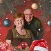 Two people standing in front of a Christmas-themed background with ornaments and lights.