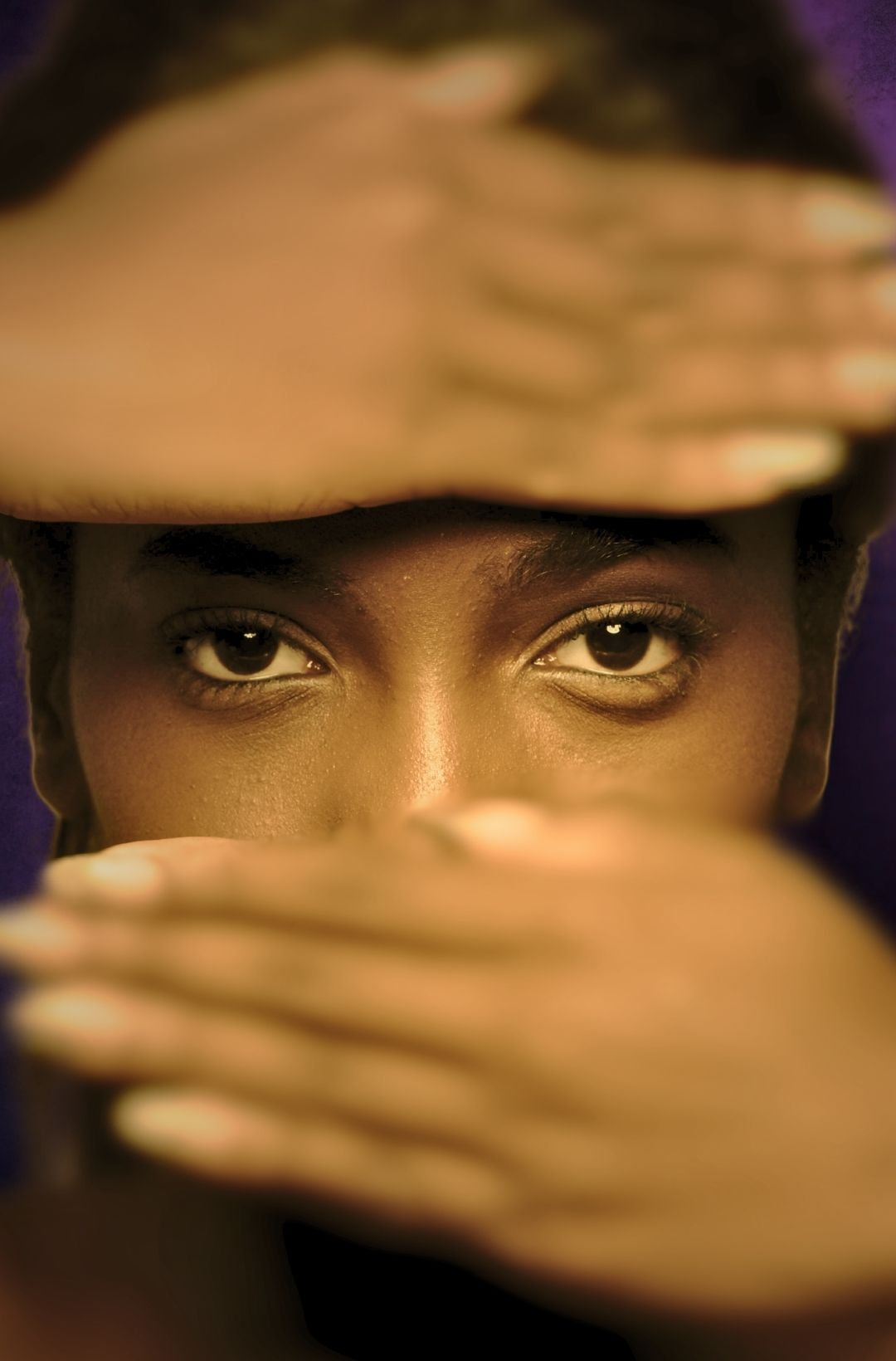 Close-up of a person covering their face with their hands while leaving the eyes visible 