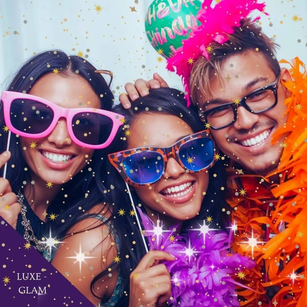 Three people with colorful sunglasses and festive hats, posing together with confetti and 'Happy Birthday' balloons.