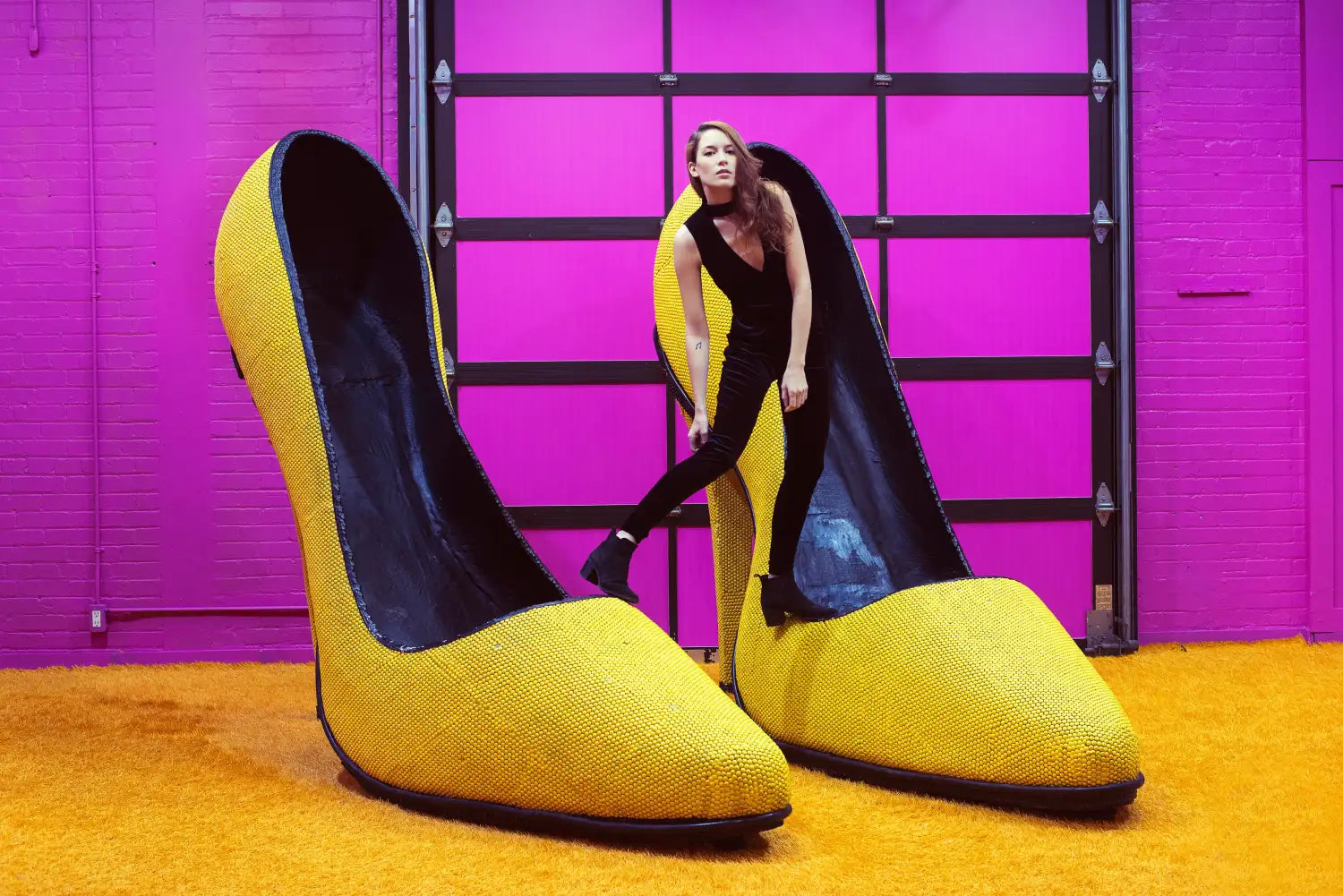 woman standing on a giant pair of yellow pumps with a hot pink background.