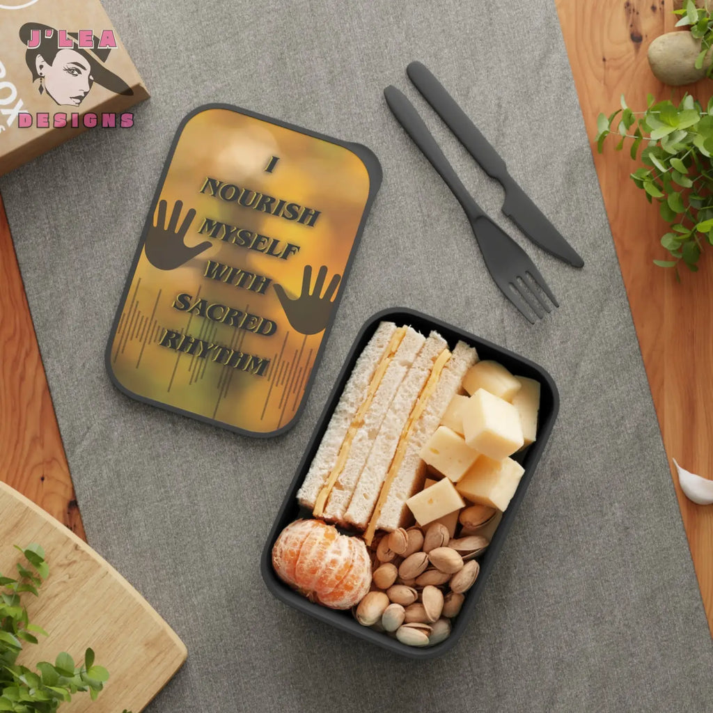 Decorative bento box with cheese, crackers, nuts, and fruit on a gray surface with a decorative mat and cutlery.