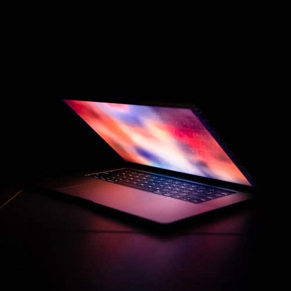 a glowing laptop sitting open surrounded by darkness 